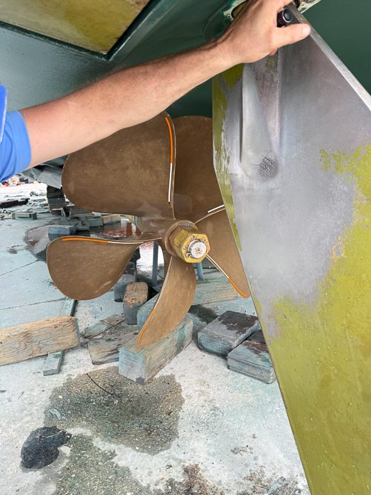 A hand on the rudder of a hauled vessel, with a bronze propeller beside it.