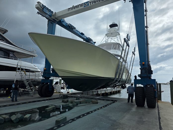 A sportfishing boat suspended in a boatyard travel lift for haul-out inspection.