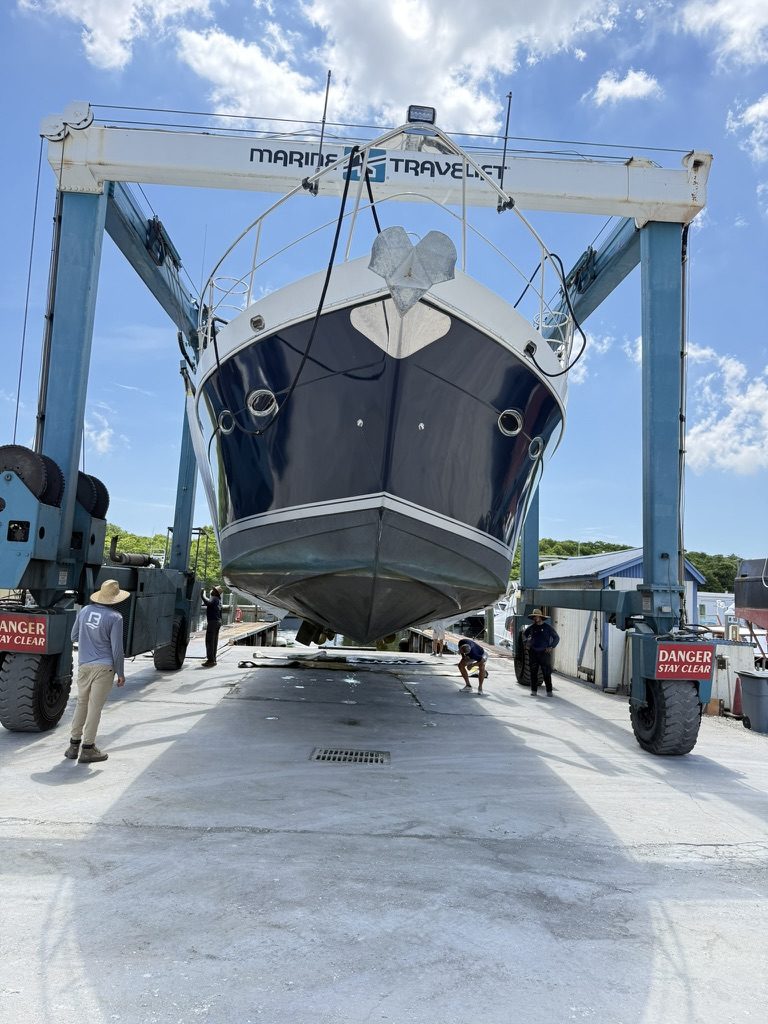 A motor yacht suspended bow-on in a Marine Travelift, yard workers standing beneath the exposed hull.